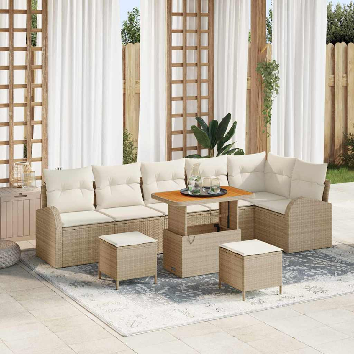 Set divano in rattan da esterno con cuscini, tavolino e pouf su un tappeto fantasia, vicino a tende bianche.