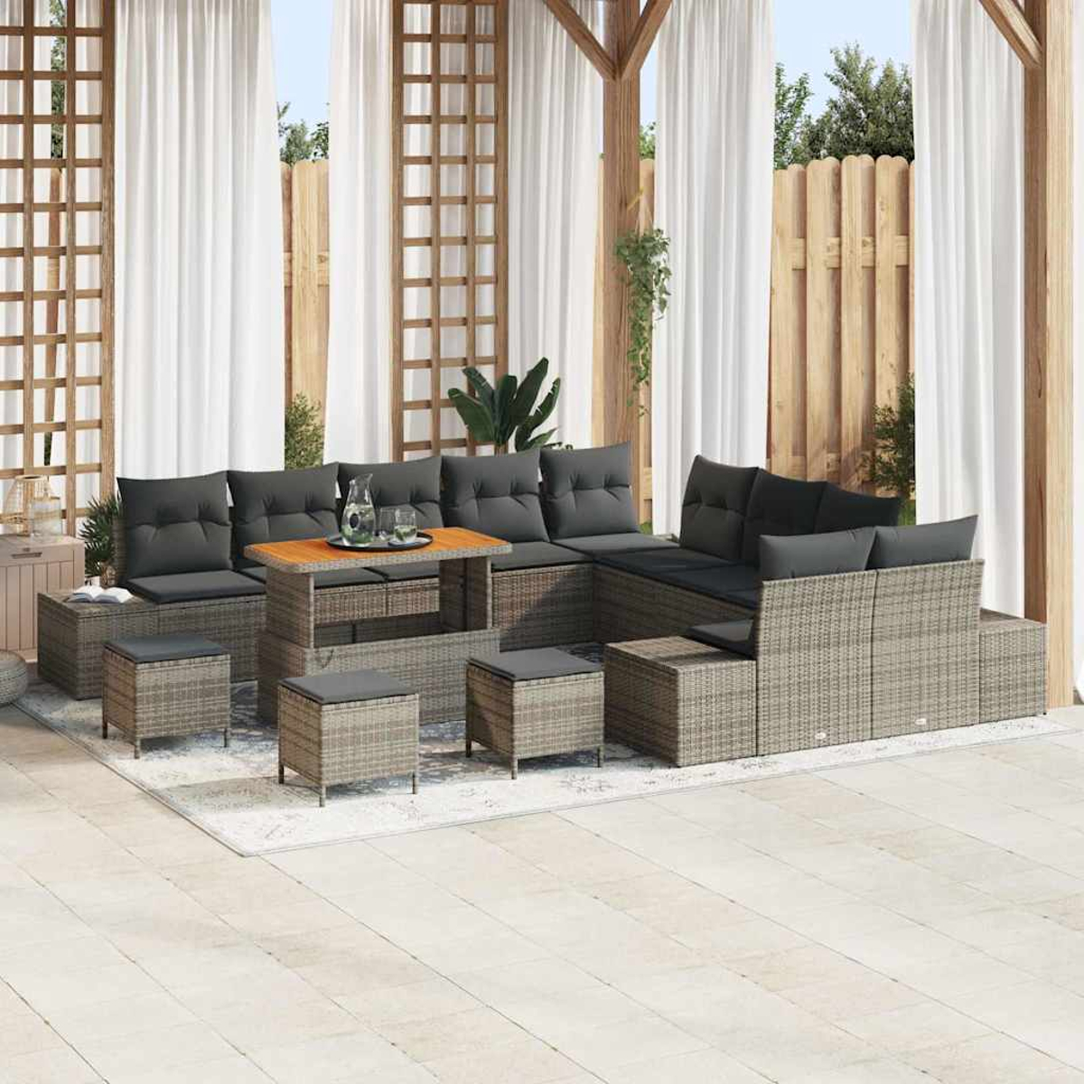 Outdoor-Terrassenset mit grauen Kissen. Enthält Sofa, Hocker und einen Holztisch. Weiße Vorhänge und Holzzaun im Hintergrund.
