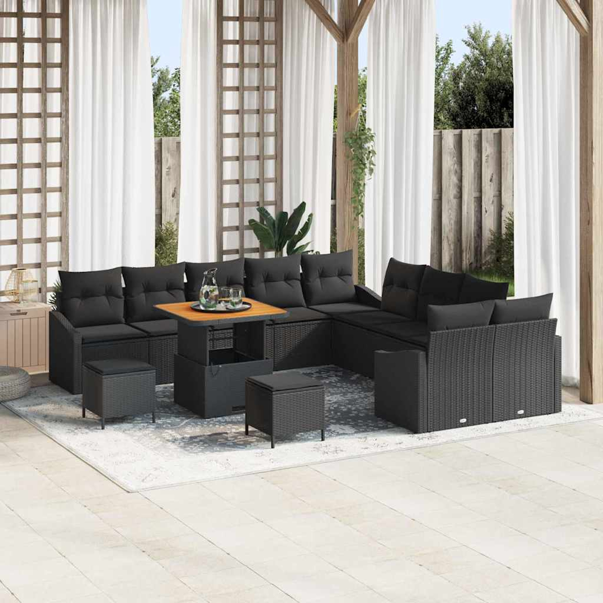 Outdoor-Terrassenmöbel-Set mit schwarzen Kissen und Rattan-Design. Enthält einen Tisch mit Getränken und Sitzgelegenheiten. Weiße Vorhänge im Hintergrund.
