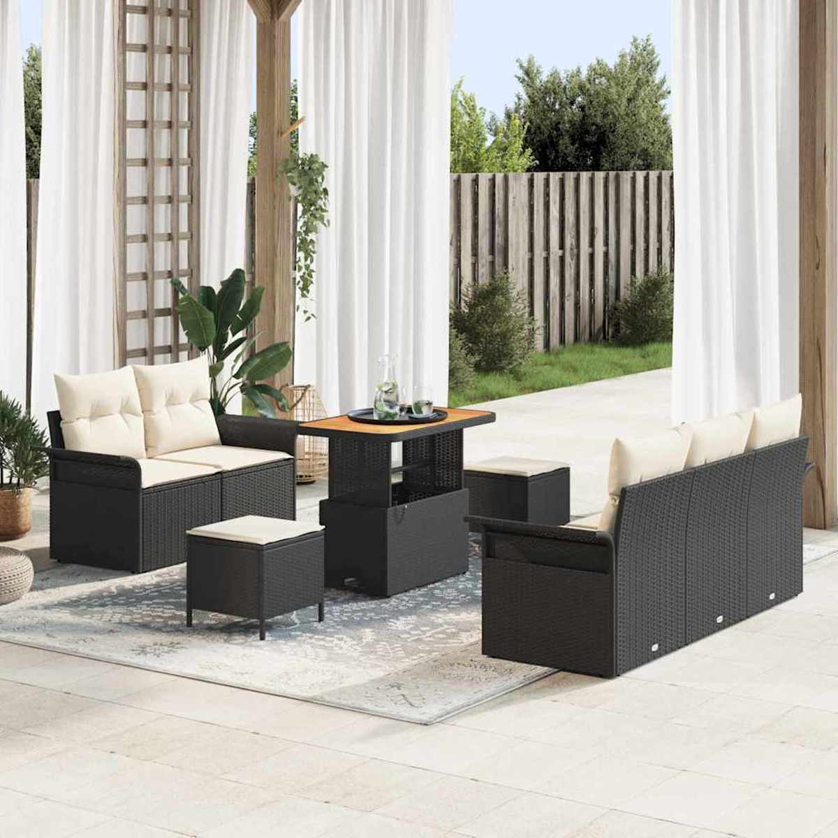 Garten-Set mit schwarzem Korbmöbeln, beigen Kissen, einem Tisch und Ottomanen auf einem gemusterten Teppich, mit weißen Vorhängen.