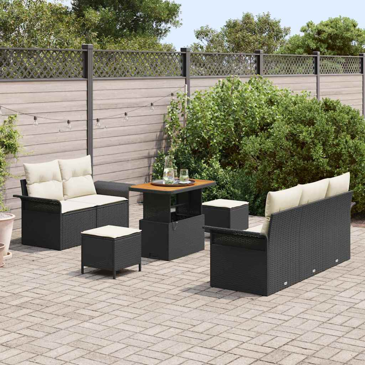 Garten-Set: schwarze Korbmöbel mit beigefarbenen Kissen, Tisch und Ottomanen auf einer Ziegelterrasse, mit einem Zaun im Hintergrund.