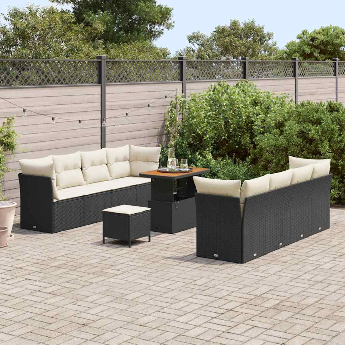 Terrassenset mit schwarzer Korbmöbeln, beigen Kissen, kleinem Tisch mit Getränken und einem Zaun im Hintergrund.