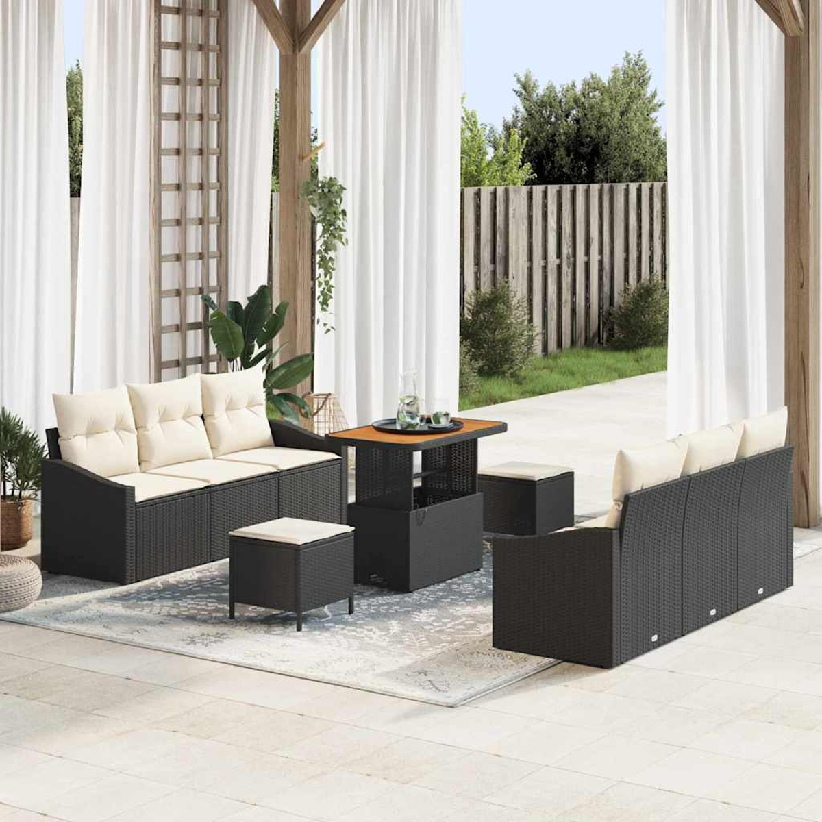 Gartenmöbel-Set mit schwarzen Korbsesseln, cremefarbenen Kissen, einem Tisch und Hockern. Weiße Vorhänge und ein Holzzaun im Hintergrund.