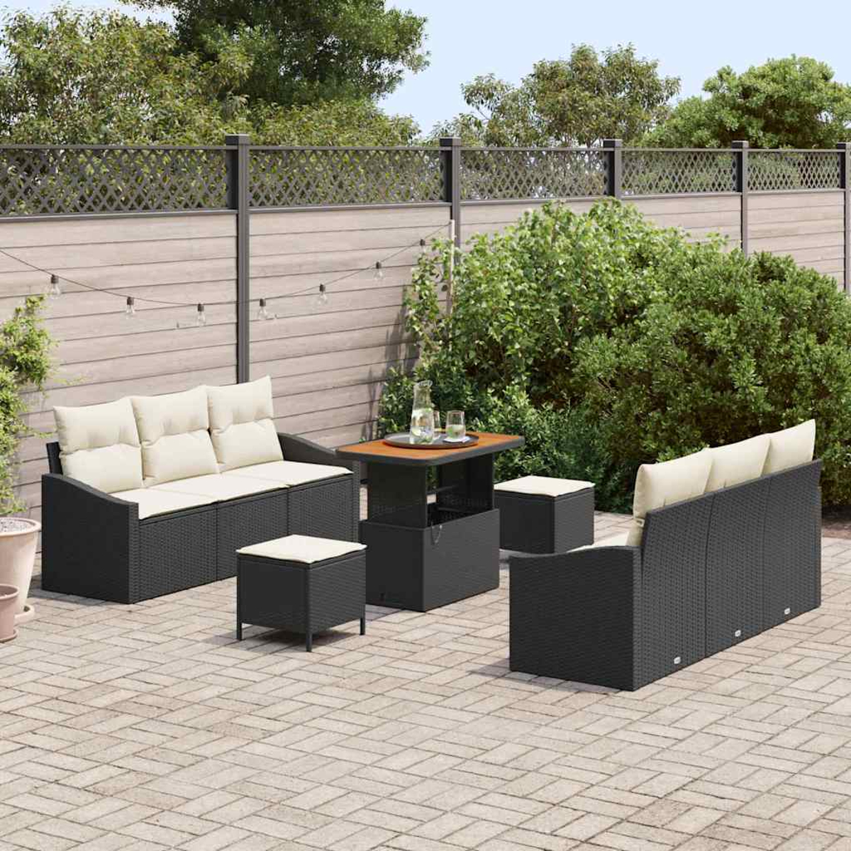 Gartenmöbel-Set: schwarze Korbsessel und Hocker mit cremefarbenen Kissen, kleiner Tisch und Holzzaun im Hintergrund.