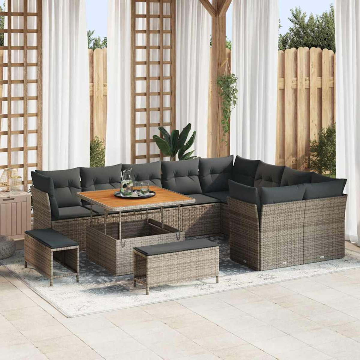 Gartenmöbel-Sitzgruppe aus Korbgeflecht mit grauen Kissen und Holztisch auf einem gemusterten Teppich.