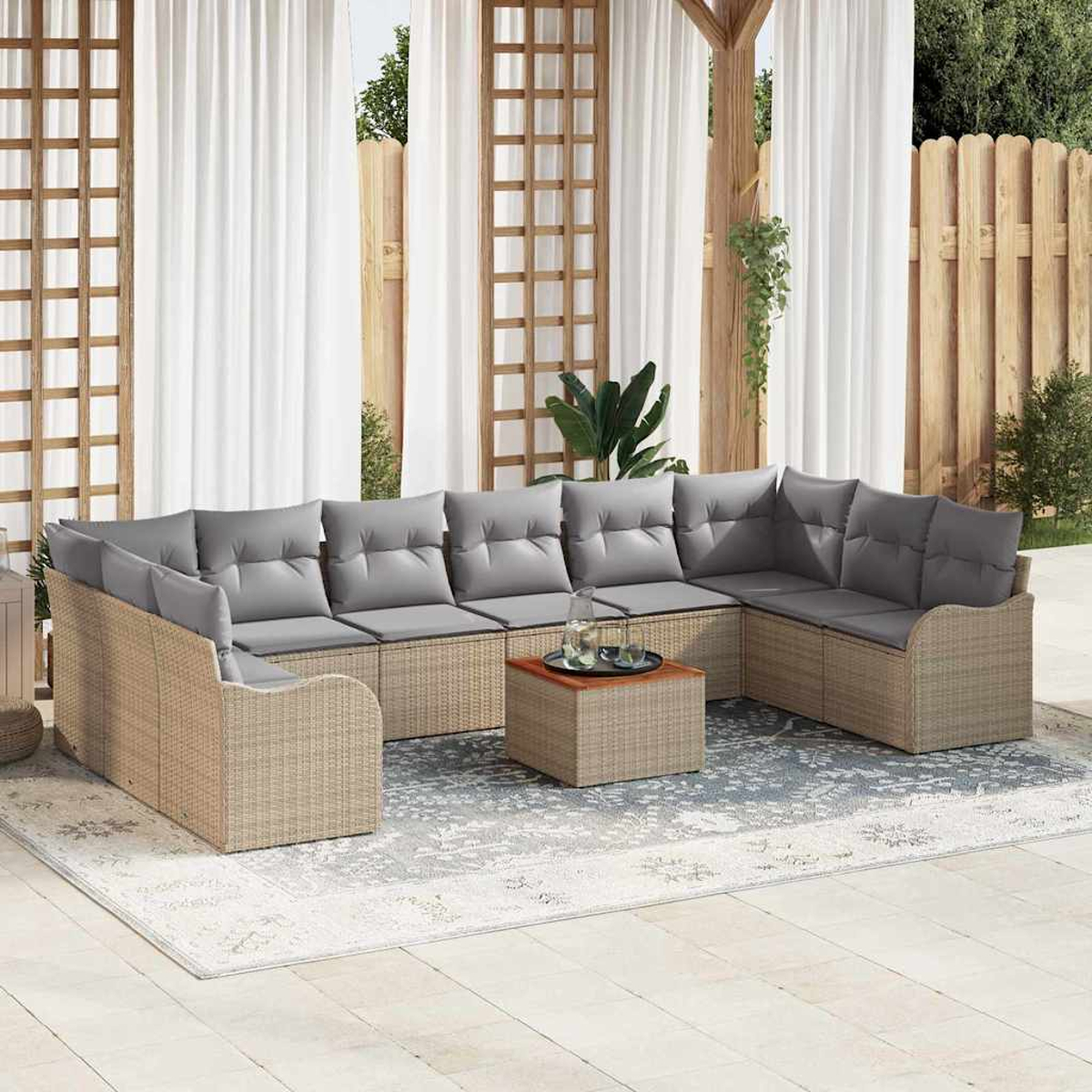 Ein Ecksofa im Freien mit grauen Kissen auf einem Teppich. Vorne steht ein Holztisch mit Getränken. Weiße Vorhänge im Hintergrund.
