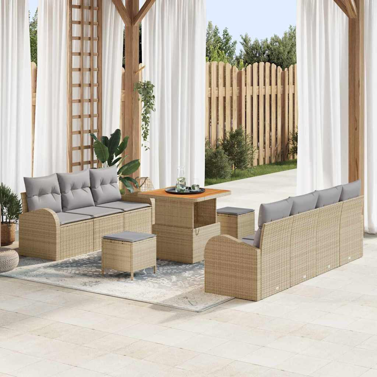 Gartenmöbel-Set. Beige Korbsessel mit grauen Kissen, Tisch und Ottomanen. Weiße Vorhänge und ein Holzzaun im Hintergrund.