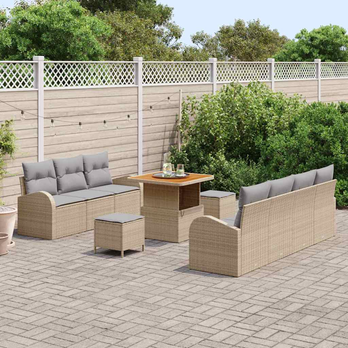 Garten-Set mit beigen Korbmöbeln, grauen Kissen, Holztisch und weißem Zaun in einem Hinterhof.