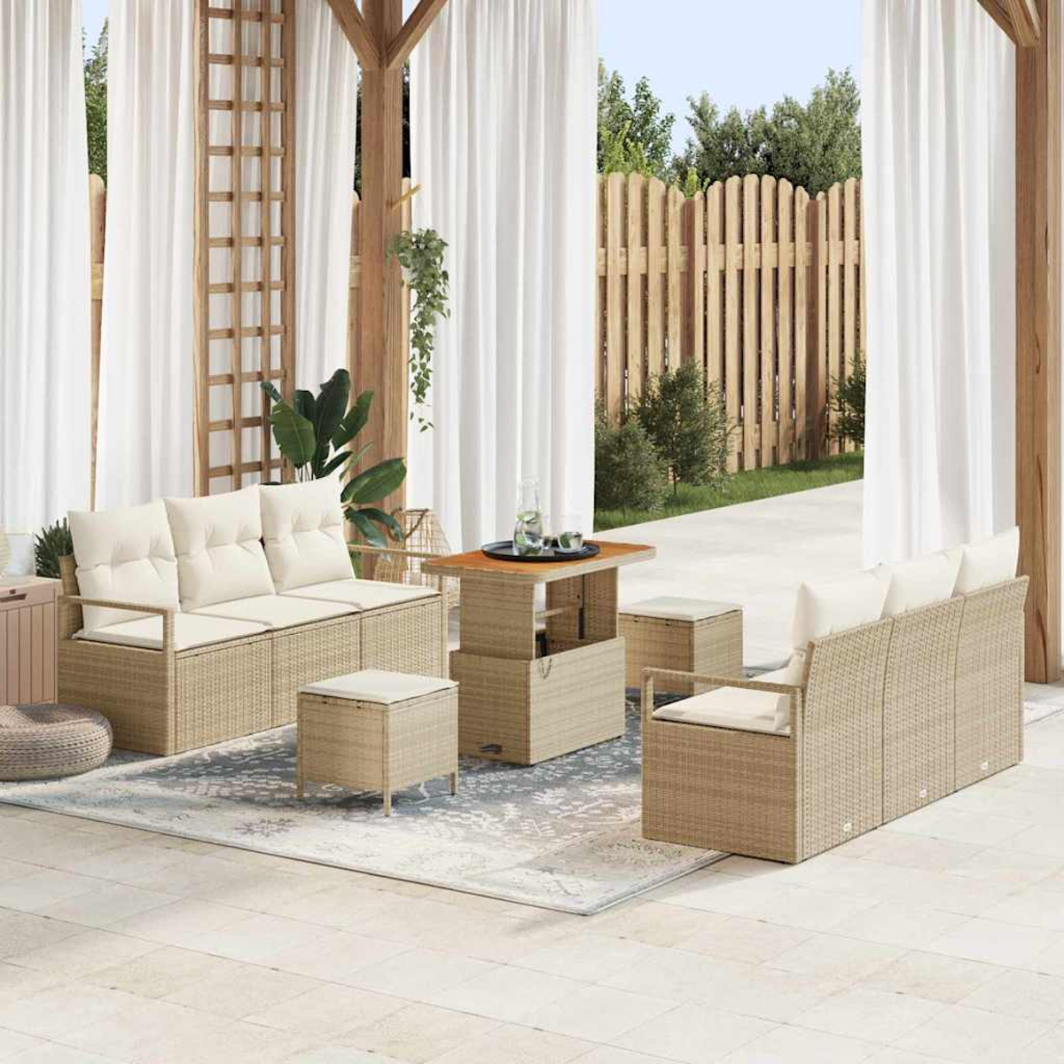 Terrassenset mit gewebten beigefarbenen Möbeln, cremefarbenen Kissen und einem Holztisch. Weiße Vorhänge und ein Holzzaun im Hintergrund.