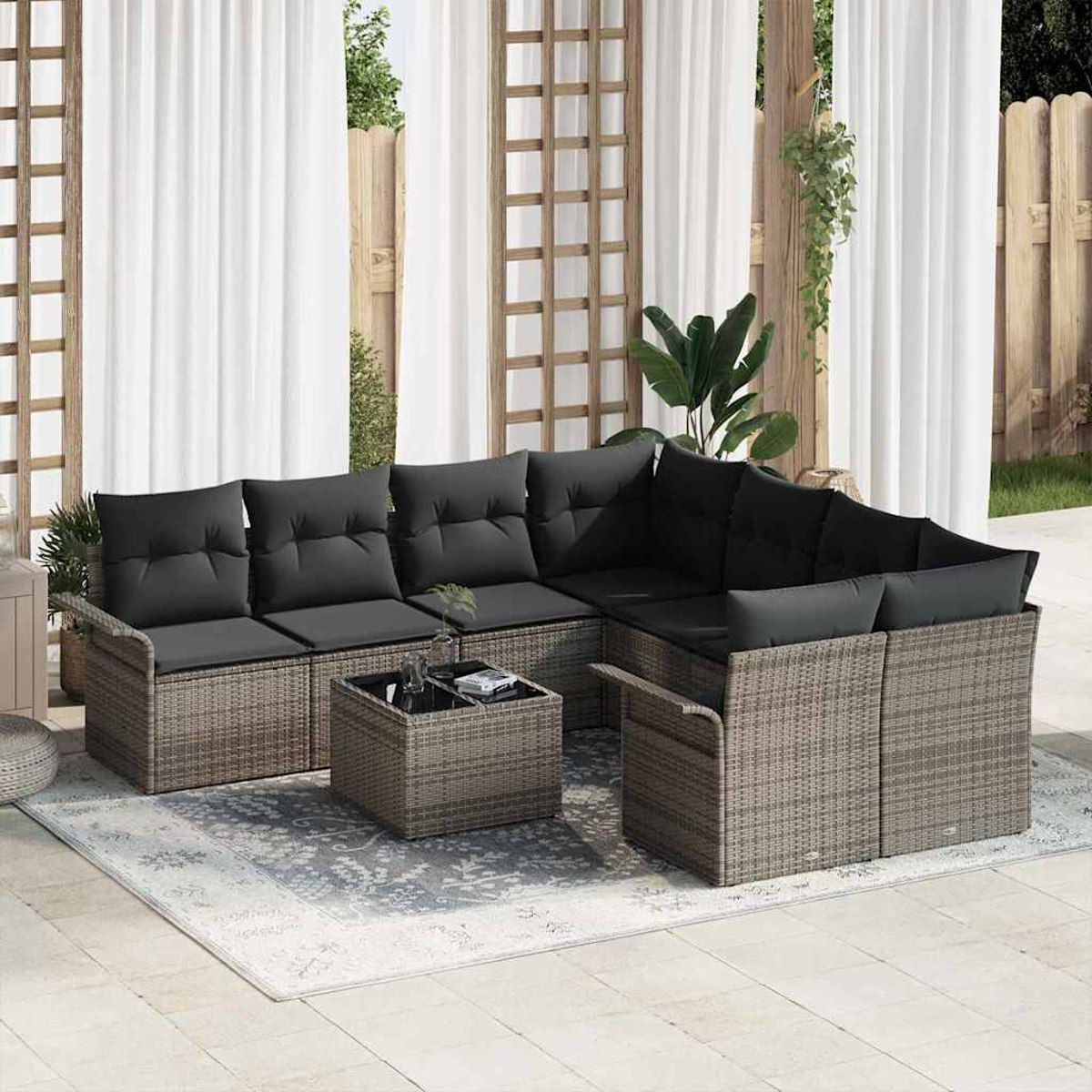 Ein Ecksofa mit schwarzen Kissen und einem Couchtisch im Freien steht auf einem Teppich. Im Hintergrund sind transparente Vorhänge zu sehen.