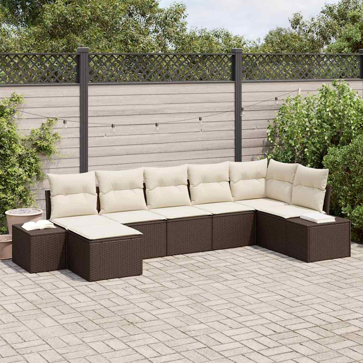 Un sofá seccional para exteriores con cojines crema. Se encuentra en un patio pavimentado frente a una valla de madera y plantas verdes.