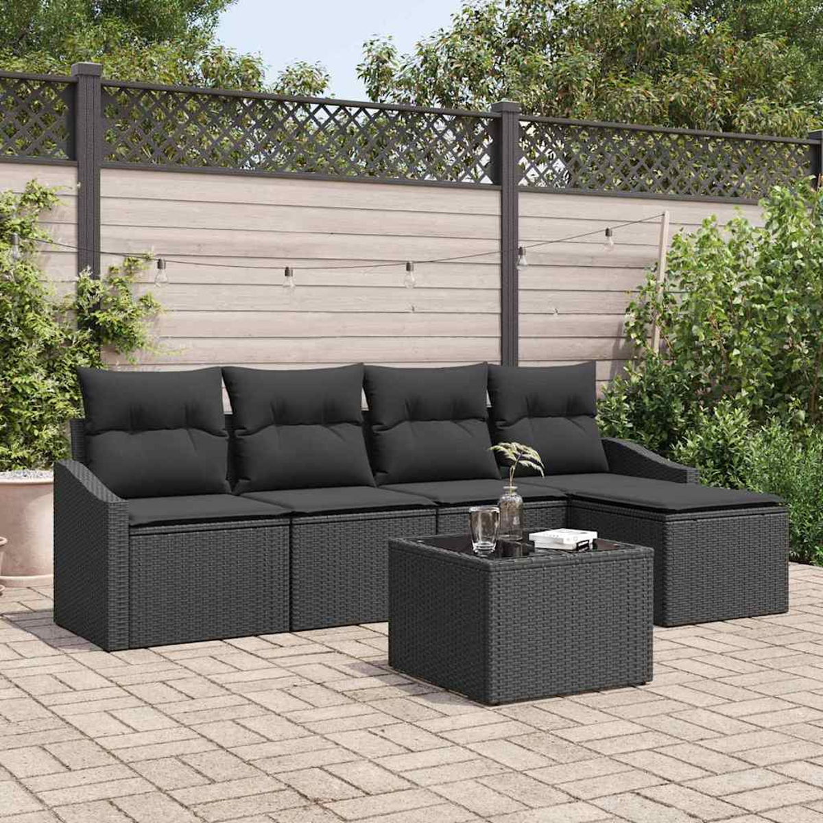 Szene im Freien mit dunkelgrauen Korbmöbeln. Ein Sofa, eine Ottomane und ein Tisch stehen auf einer Ziegelterrasse, mit einem Holzzaun im Hintergrund.