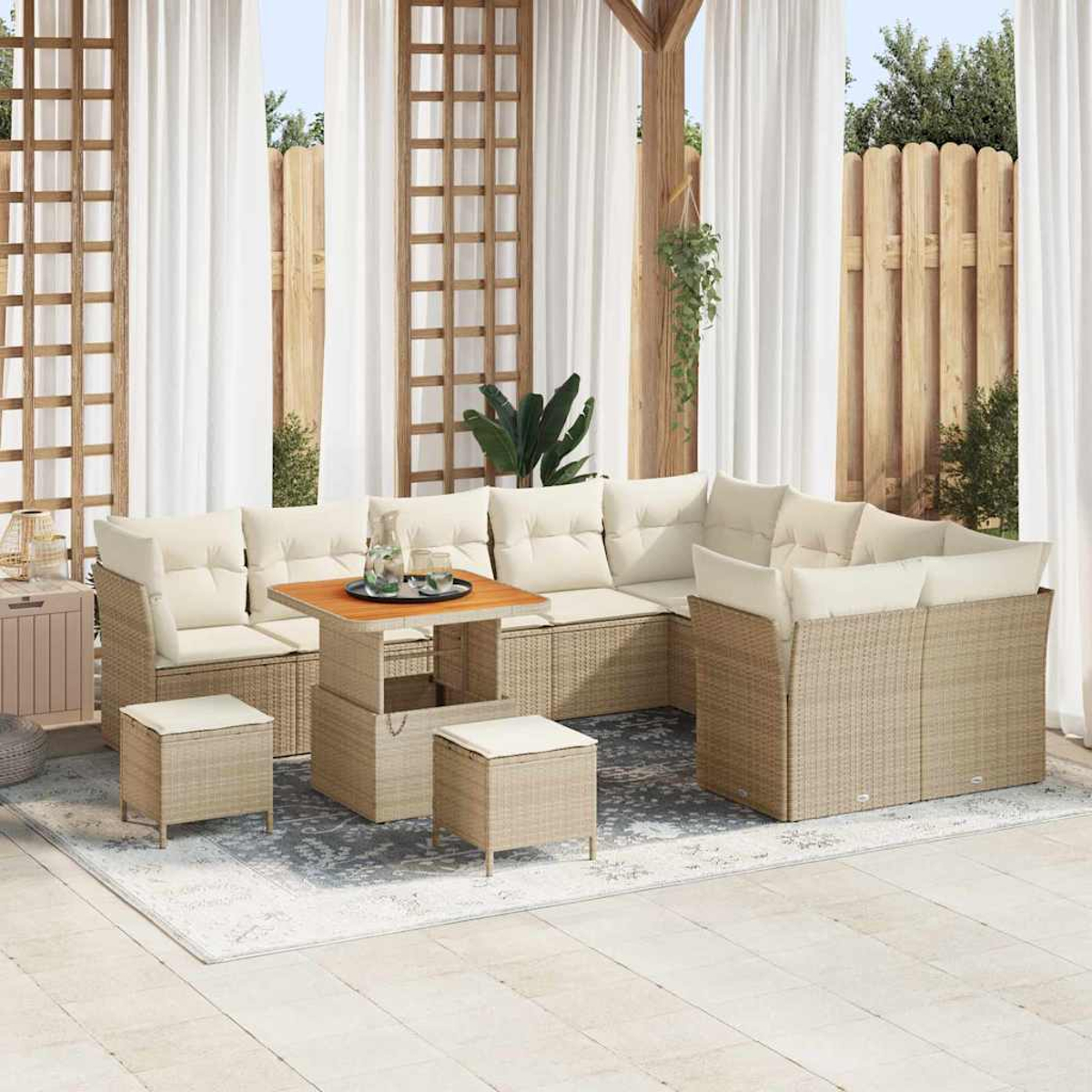 Outdoor-Terrassenset mit beigefarbenen Kissen, einem Holztisch und passenden Hockern auf einem gemusterten Teppich, Vorhängen und Holzgitter im Hintergrund.