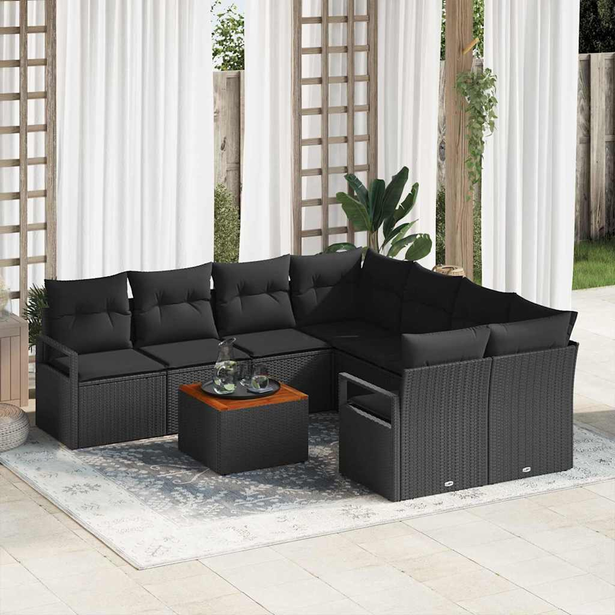Gartenmöbel-Set: schwarzes Korbsofa mit Kissen, ein kleiner Tisch und weiße Vorhänge im Hintergrund.