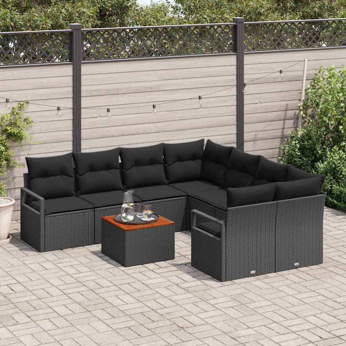 Garten-Set mit schwarzen Kissen auf grauen Korbmöbeln, einem kleinen Tisch und einem Zaun im Hintergrund mit Pflanzen.