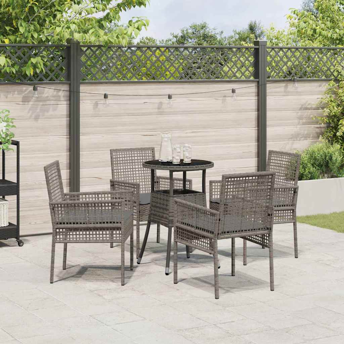 Garten-Terrassenset. Graue Stühle um einen kleinen Tisch mit Krug und Gläsern. Holzzaun im Hintergrund. Grün und klarer Himmel.