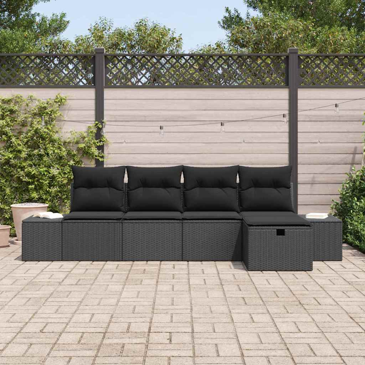 Gartenmöbel-Set. Dunkelgraues Korbmöbel-Sofa mit schwarzen Kissen. Im Hintergrund ein Holzzaun und Pflanzen.