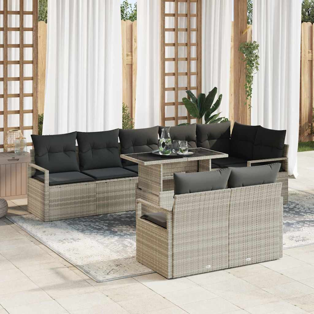 Terrassenset mit grauen Kissen. Es hat einen Tisch, zwei Sofas und zwei Stühle auf einem Teppich. Weiße Vorhänge im Hintergrund.