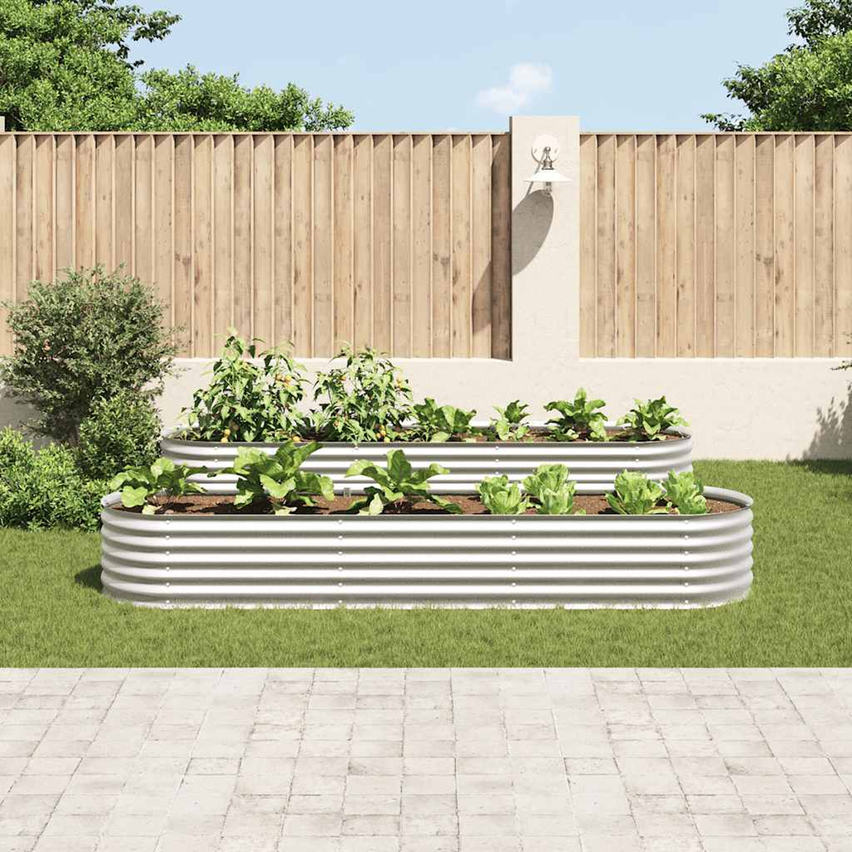 Zwei erhöhte Metall-Gartenbeete mit Gemüse. Im Hintergrund ein Holzzaun und eine hellfarbige Wand. Grünes Gras und Steinterrasse.