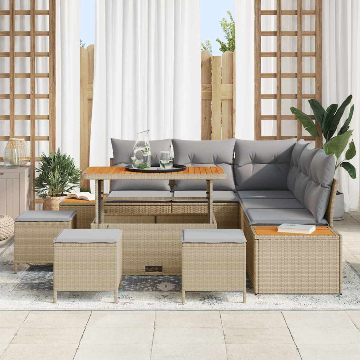 Outdoor-Rattanmöbelset mit grauen Kissen, Holztisch mit Tablett und Hockern. Vorhänge und Pflanzen im Hintergrund.