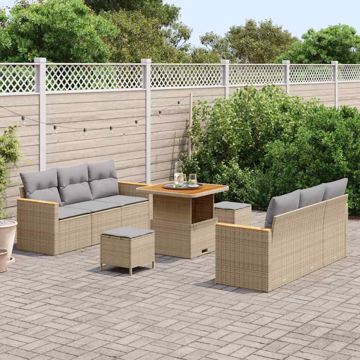 Garten-Sitzgruppe mit Sofa, zwei Stühlen, Tisch und Hocker. Auf einer gepflasterten Terrasse mit Zaun und Grün im Hintergrund.