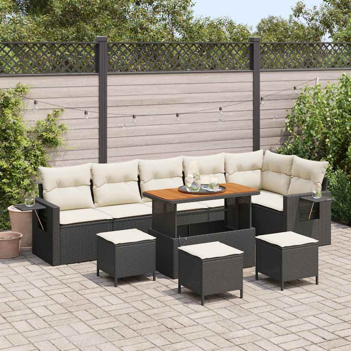 Terrassenset mit Sofa, Tisch und Hockern. Beige Kissen, dunkelgraue Rahmen, Tischplatte aus Holz, auf einer Ziegelterrasse, mit Zaun.