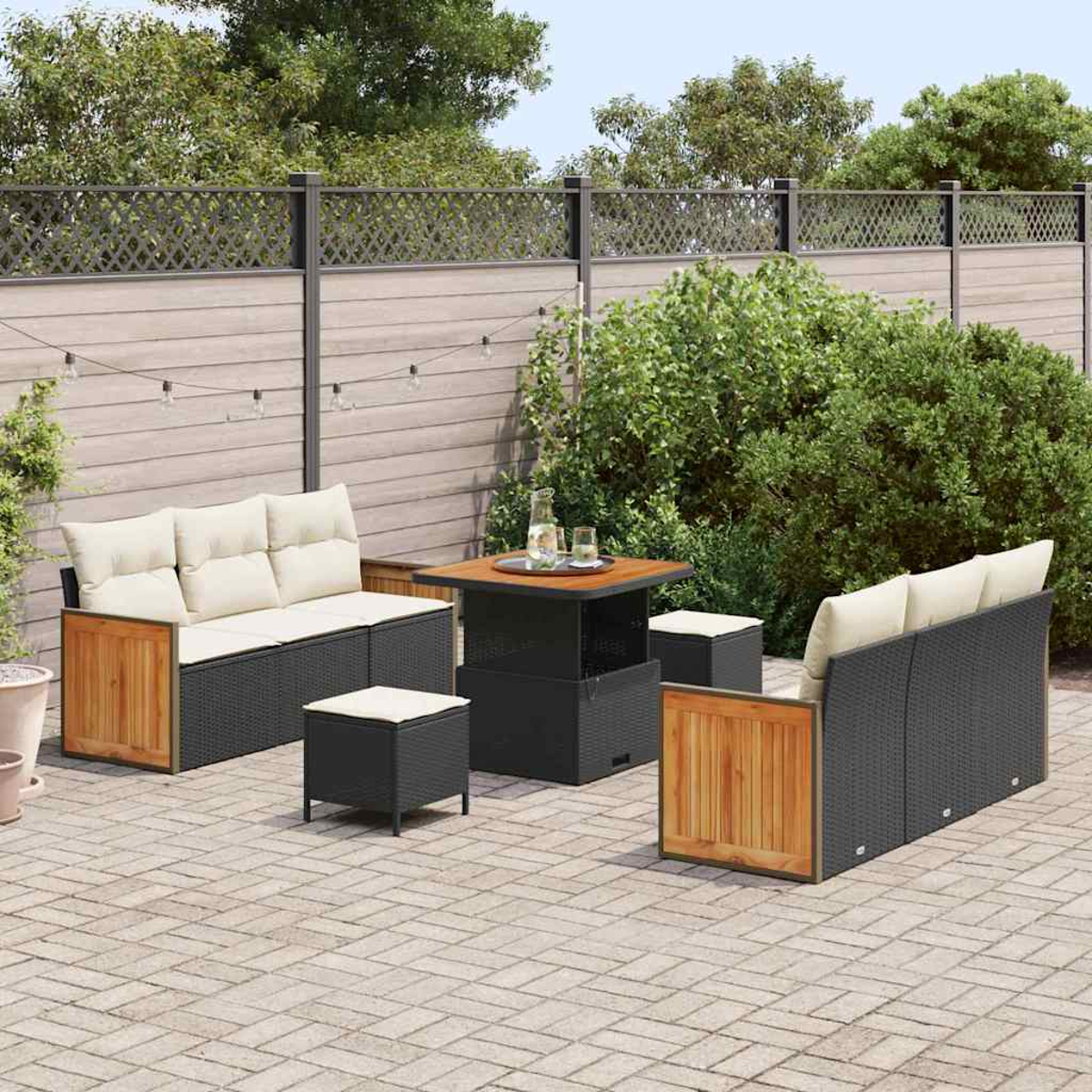 Set da patio esterno con divano, tavolo e pouf su un patio in mattoni, circondato da una recinzione e vegetazione.