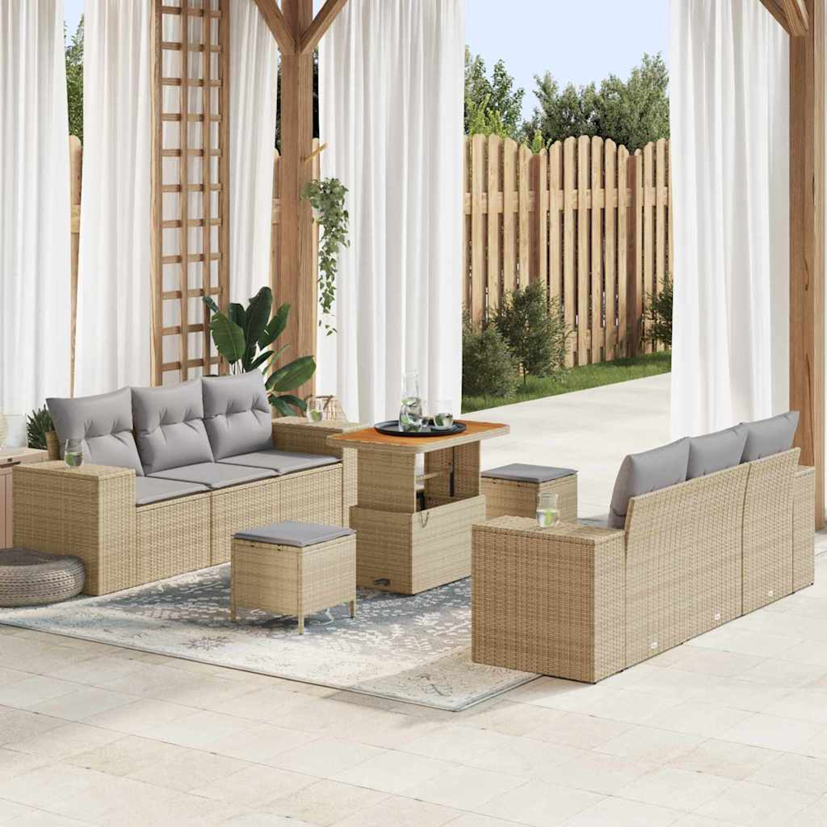 Terrassenmöbel-Set mit Korbsesseln, grauen Kissen, einem Tisch und Ottomanen, alles auf einem Teppich. Weiße Vorhänge und Holzzaun.