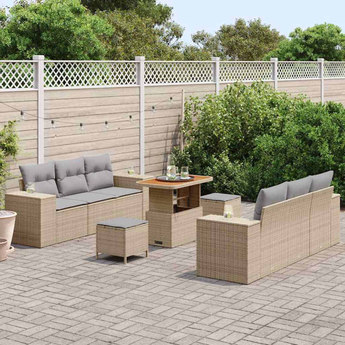 Gartenmöbel-Set auf einer Terrasse. Enthält zwei Sofas, einen Tisch und zwei Ottomane. Graue Kissen und beige gewebte Rahmen. Grüner Hintergrund.