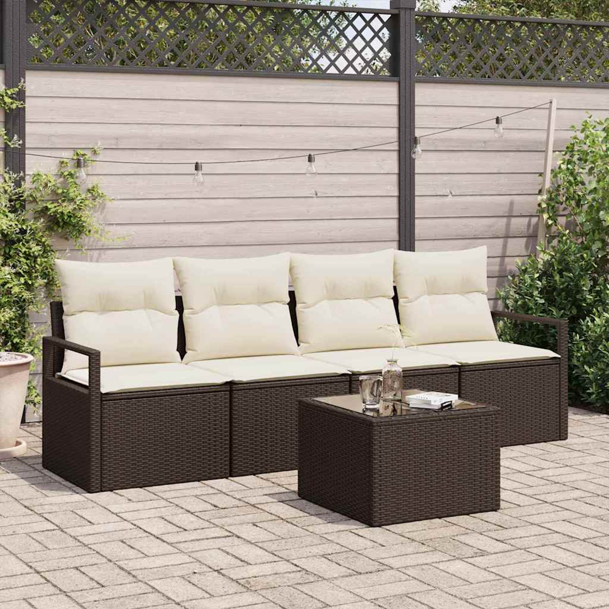 Terrassenset im Freien mit dunkelbraunen Korbmöbeln, cremefarbenen Kissen und einem Couchtisch mit Glasplatte. Vor einem Holzzaun.