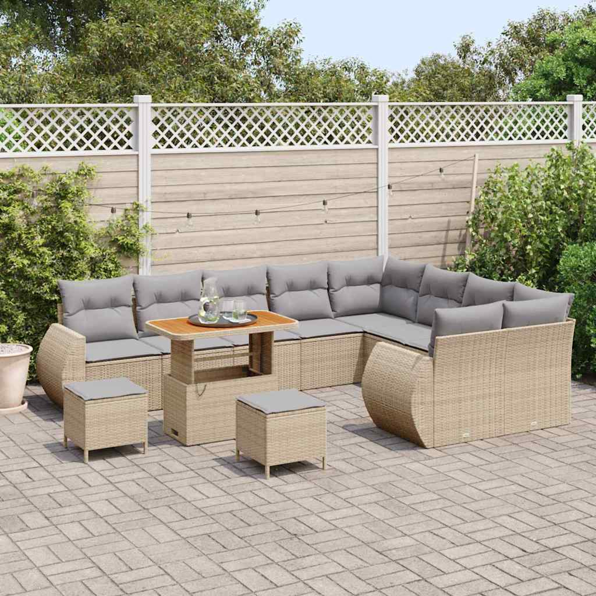 Terrassenset mit Korbmöbeln und grauen Kissen. Enthält einen Tisch, ein Ecksofa und zwei Ottomanen auf einer gepflasterten Terrasse.