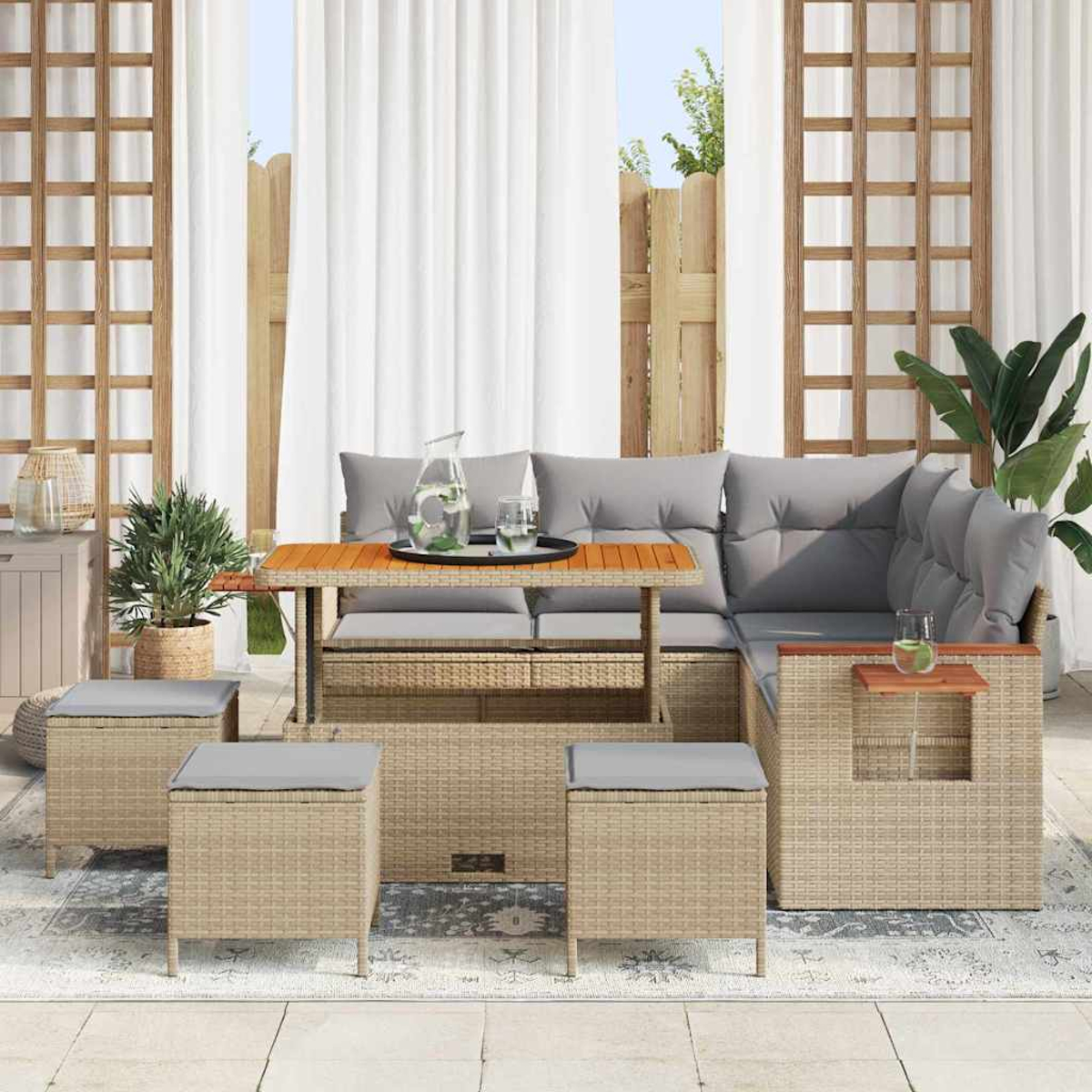 Terrassen-Set mit Rattan-Sofa, Tisch und Hockern. Graue Kissen und ein Glas Wasser auf dem Tisch. Im Hintergrund Vorhänge und Pflanzen.