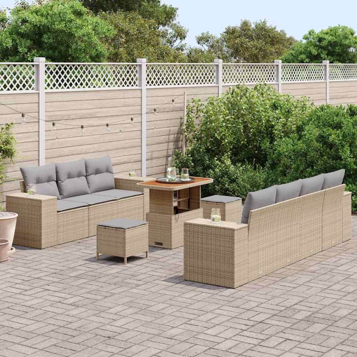 Juego de patio al aire libre. Muebles de mimbre beige con cojines grises. Incluye un sofá, dos sillas, una mesa y un pequeño otomano en un patio de piedra.
