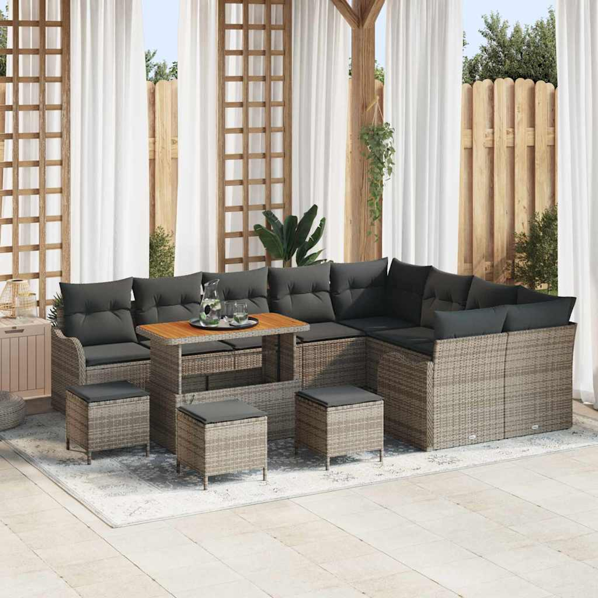 Outdoor-Ecksofa-Set mit Kissen, Tisch und Hockern auf einem Teppich. Weiße Vorhänge und Holzzaun im Hintergrund.