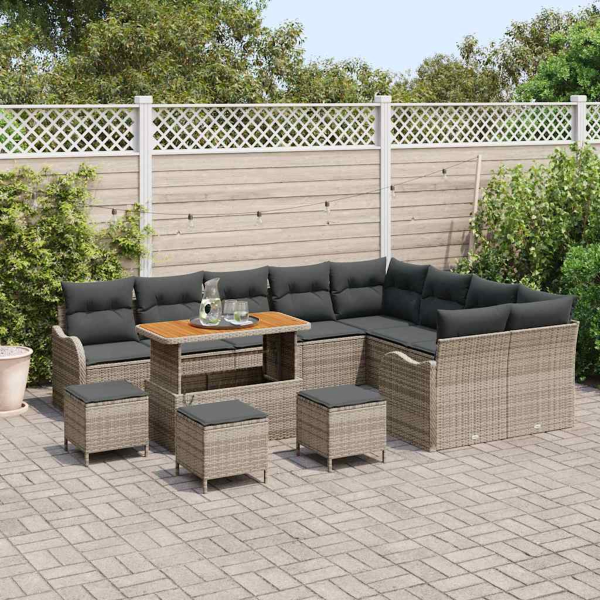 Gartenmöbel-Set: Ecksofa, Tisch und Hocker. Graue Kissen, hellbraunes Korbgeflecht, Holztisch. Auf Stein gepflastert.