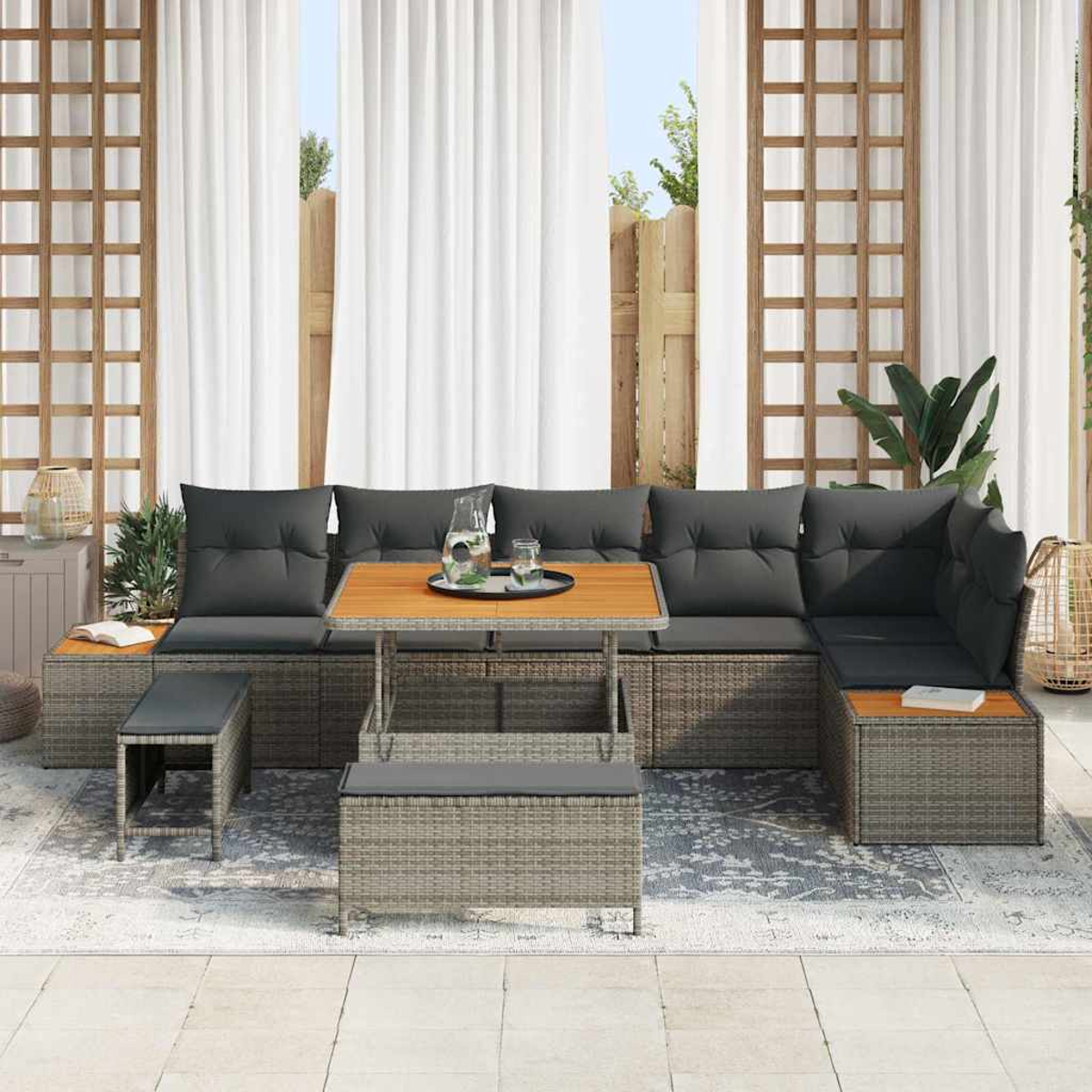 Set da patio esterno con cuscini grigi, tavolo in legno e sedute in tessuto grigio. Tende bianche e un traliccio in legno sullo sfondo.