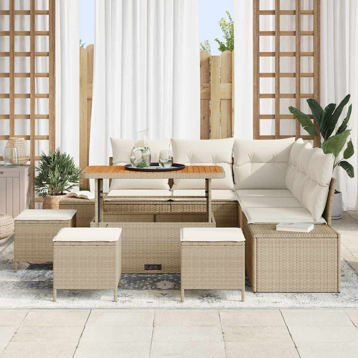Set di sedute da esterno in stile rattan. Include un tavolo, un divano componibile e pouf con cuscini bianchi. Sfondo con tende e piante.