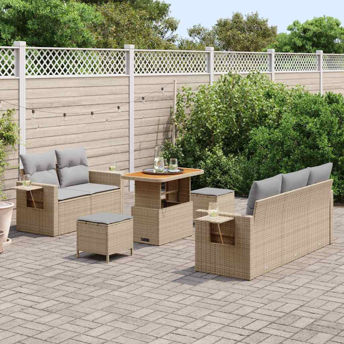 Terrassenmöbel-Set mit Sofa, Stühlen, Tisch und Ottomane. Graue Kissen und ein Holzzaun. Grüne Büsche im Hintergrund.
