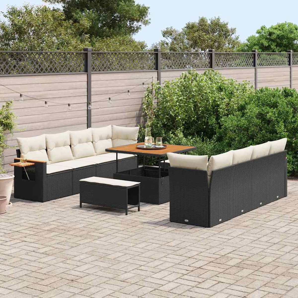 Gartenmöbel-Set mit schwarzem Korbgeflecht und cremefarbenen Kissen auf einer Backstein-Terrasse. Tisch, Sofa und Bank im Garten.