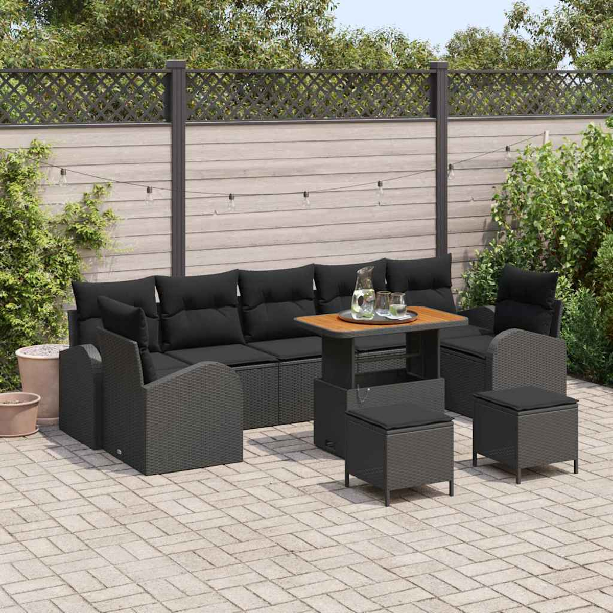 Garten-Terrassenset mit schwarzen Kissen, Tisch und Stühlen auf einer Ziegelterrasse. Im Hintergrund befinden sich ein Zaun und Grün.