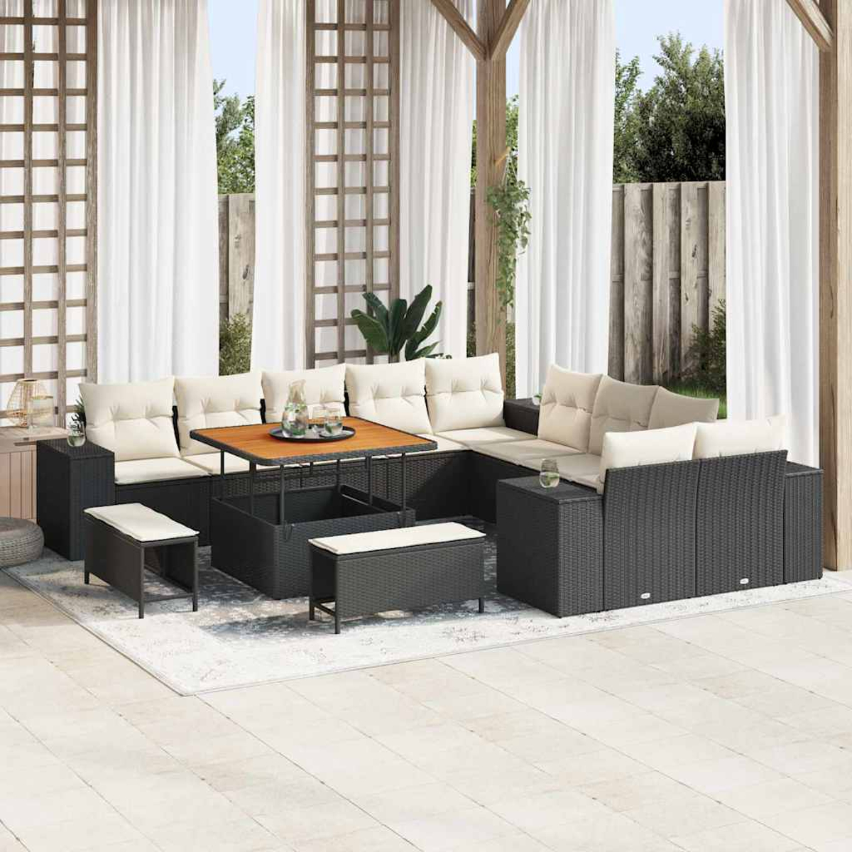 Juego de muebles de patio. Sofá de mimbre oscuro con cojines crema, mesa de café y bancos sobre una alfombra. Cortinas blancas al fondo.