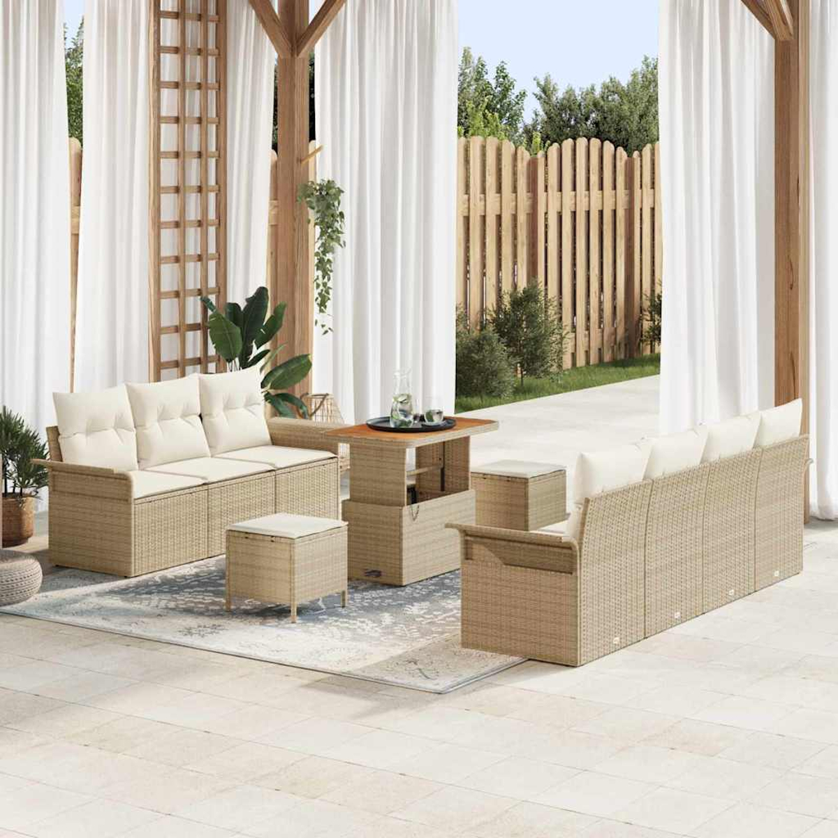 Outdoor-Sitzbereich mit beigen Korbmöbeln, weißen Kissen, einem Holztisch und weißen Vorhängen. Im Hintergrund ist ein Holzzaun.