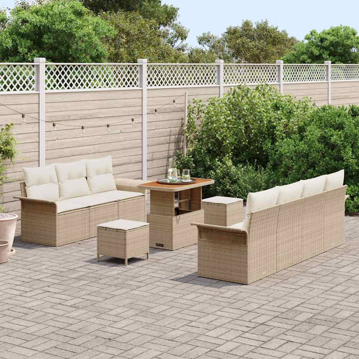 Garten-Terrassenset mit beigen Korbmöbeln und hellen Kissen. Auf einer Ziegelterrasse, mit Zaun und Grün im Hintergrund.