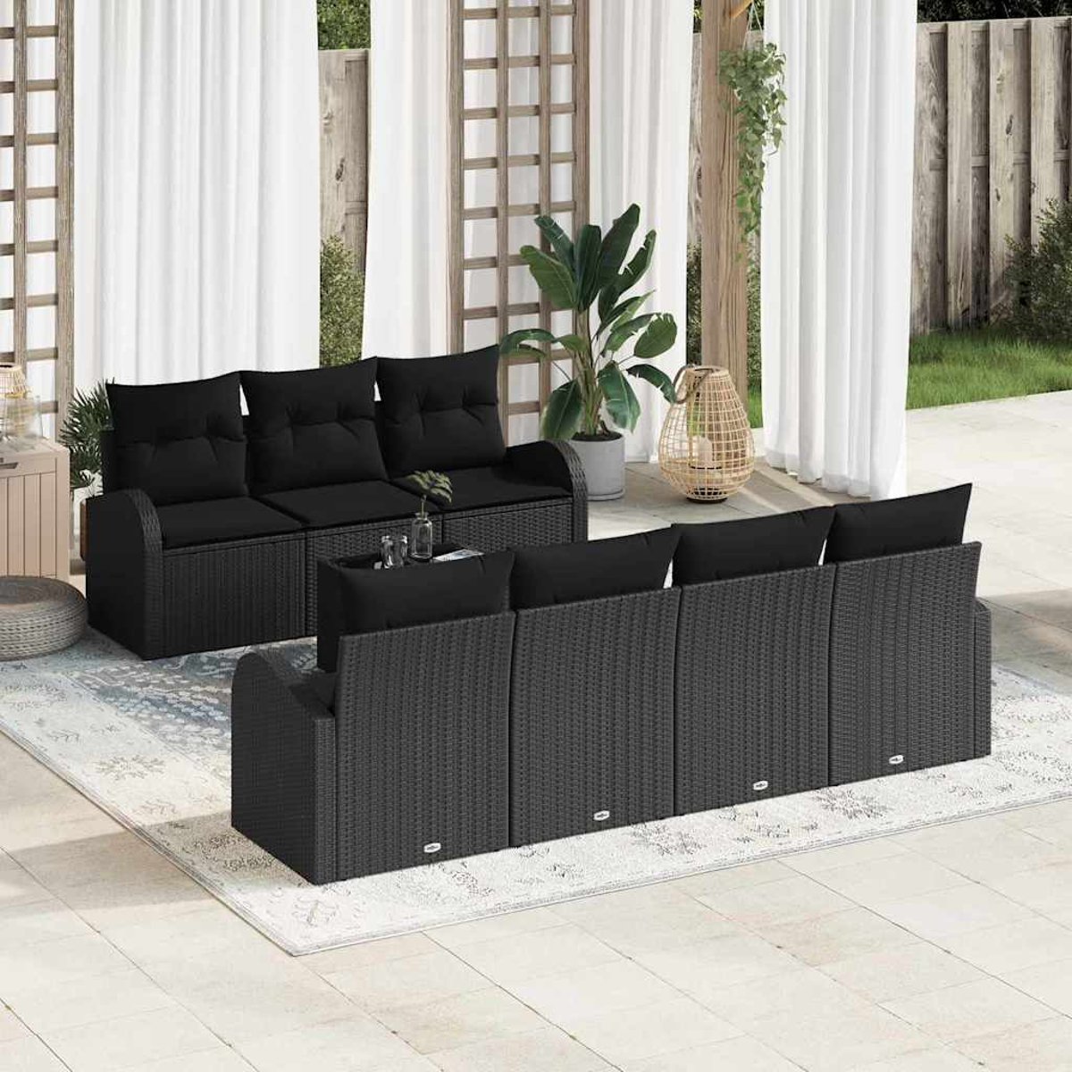 Terrassenset mit schwarzen Korbsesseln, Kissen und einem Teppich. Weiße Vorhänge, Pflanzen und Holzgitter im Hintergrund.