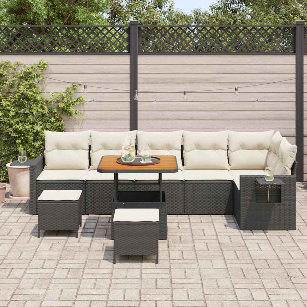 Ein Outdoor-Terrassenset mit einem grauen Rattan-Ecksofa, einem Tisch und zwei Ottomanen auf einer Backsteinterrasse, mit einem Holzzaun im Hintergrund.