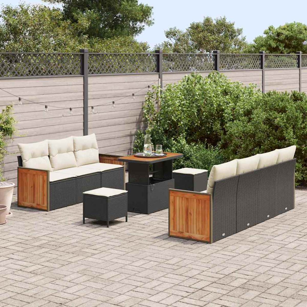 Set patio esterno con mobili in vimini grigi, dettagli in legno, cuscini beige e un tavolino. Cespugli verdi e una recinzione sullo sfondo.