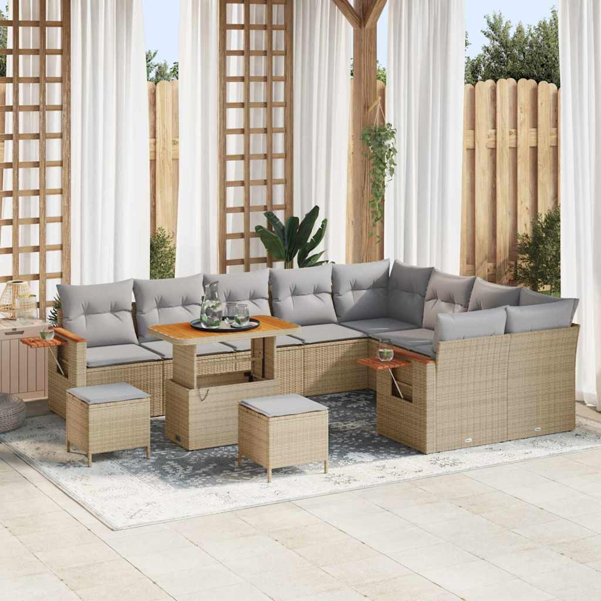 Outdoor-Rattan-Ecksofa mit grauen Kissen, Holztisch und Hockern. Weiße Vorhänge und Holzzaun im Hintergrund.