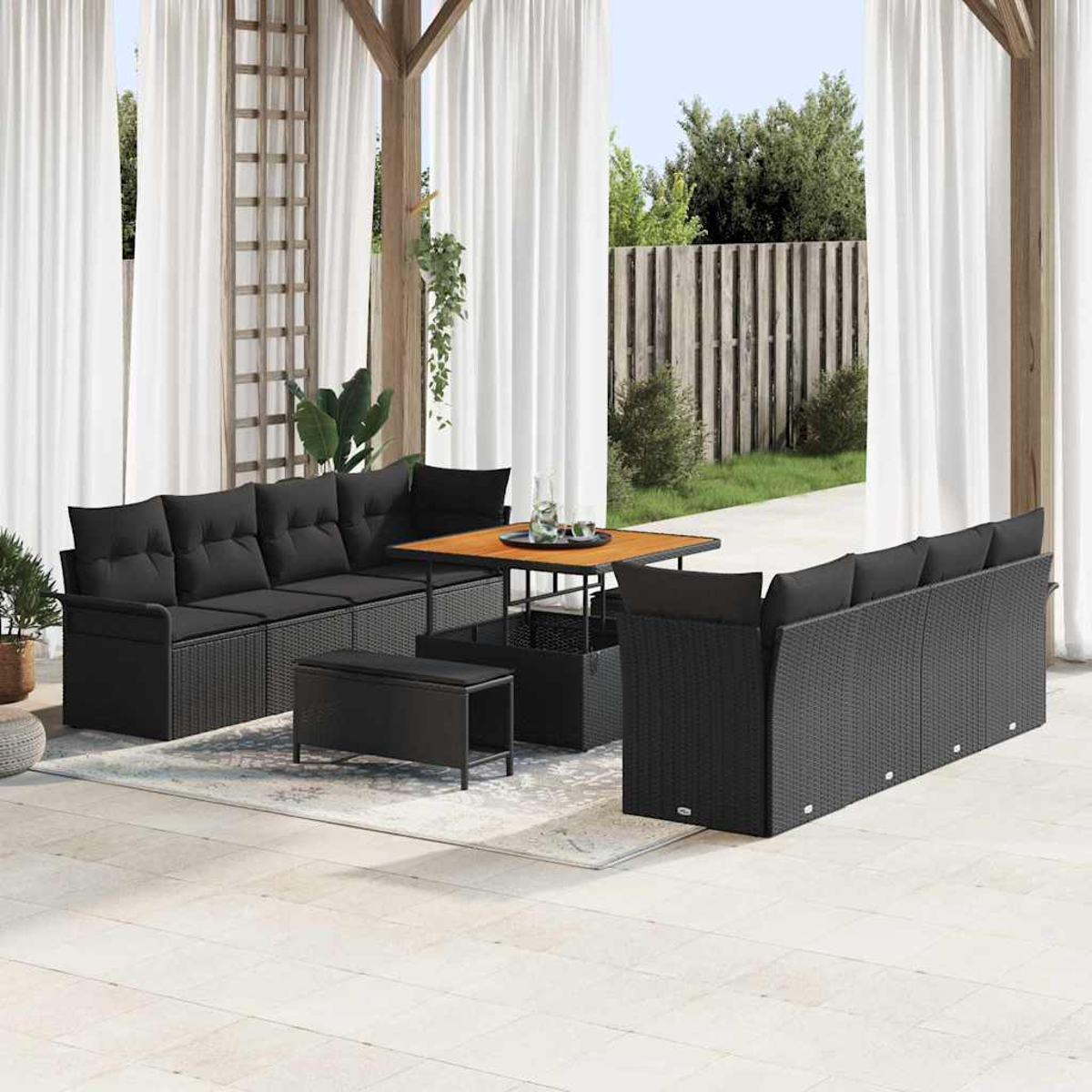 Terrassengarnitur mit schwarzen Korbsesseln, einem quadratischen Tisch und einer Bank. Weiße Vorhänge und Holzstruktur im Hintergrund.