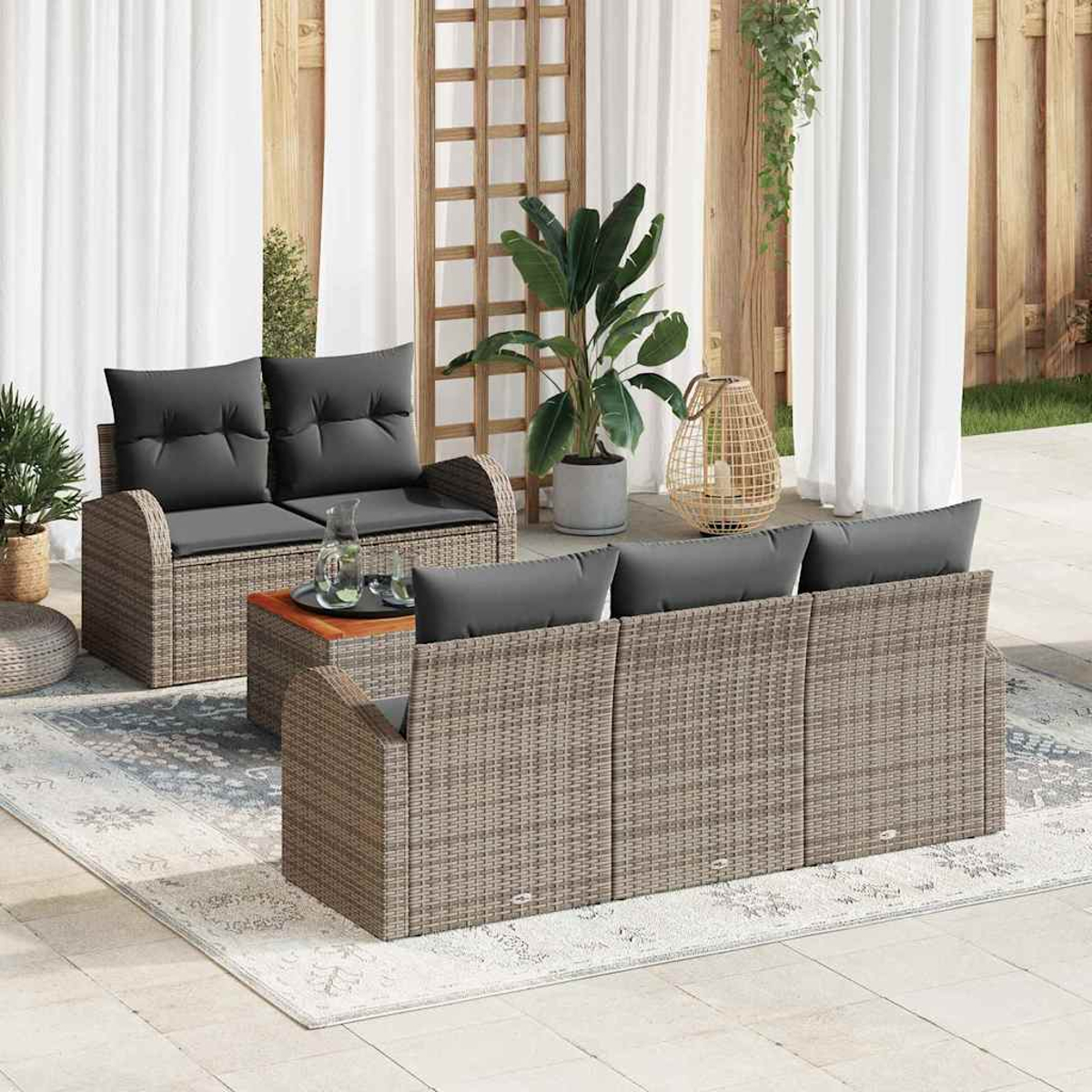 Garten-Terrassenset mit grauen Kissen, einem Couchtisch und Pflanzen. Im Hintergrund weiße Vorhänge und Holzstrukturen.