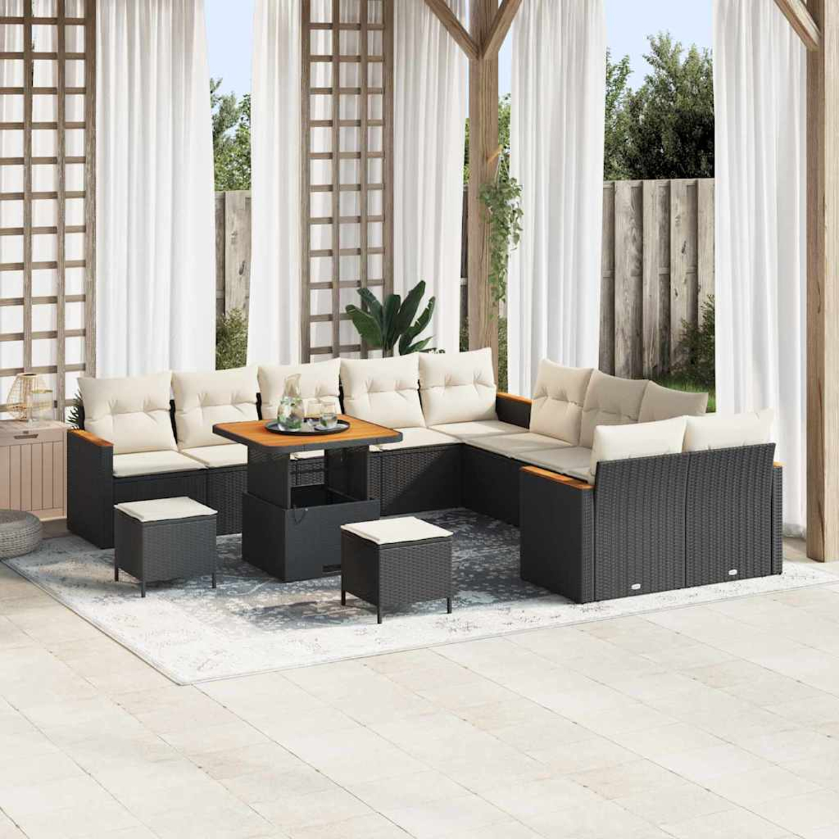 Gartenset mit schwarzen Korbsesseln, beigen Kissen, Holztisch und Hockern. Weiße Vorhänge und Spalier im Hintergrund.